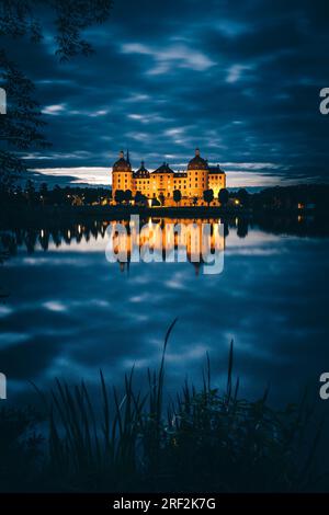 Moritzburg bei Dresden in Deutschland zur blauen Stunde. Beleuchtete Burg am Wasser im Park. Reflexion Stockfoto