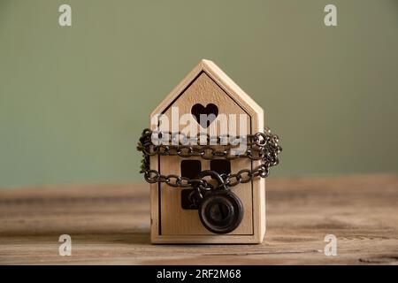 Das Haus ist mit Ketten und Vorhängeschlössern versehen und steht auf einem Holzbrett, das Konzept eines Verbots des Verkaufs von Immobilien, Hausschutz Stockfoto