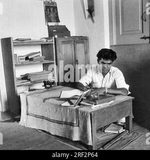 Altes schwarzweißes Bild aus dem Jahr 1900er von einem Arbeiter, der an einem Schreibtisch sitzt, Holztisch Indien 1940er Stockfoto