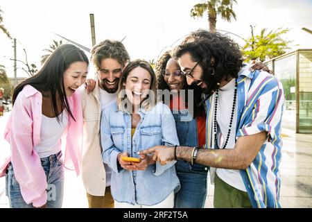 Eine vielfältige Gruppe von fröhlichen Millennials-Freunden, die zusammen eine Telefonstraße beobachten. Fröhliche, multiethnische, junge, sorgenfreie Freunde, die lachen und Stockfoto