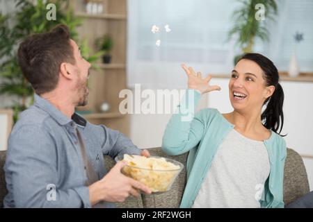 Verspielte Freundin, die Popcorn in den Mund ihrer Freunde wirft Stockfoto