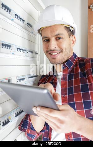 Männlicher Techniker, der den Sicherungskasten mit einem Tablet-pc untersucht Stockfoto