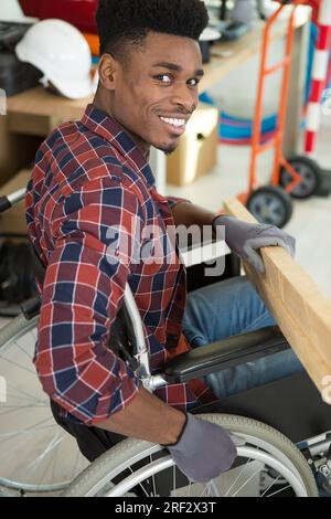 Junger Mann im Rollstuhl versucht sich selbst, sein Bücherregal zu falten Stockfoto