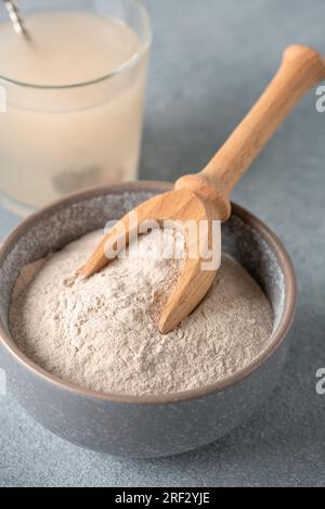 Psyllium-Strohpulver in Schüssel Nahaufnahme und Glas mit wasserlöslicher Faser für den Darm, grauer Hintergrund. Glutenfreies Diätkonzept. Seitenansicht, Sele Stockfoto