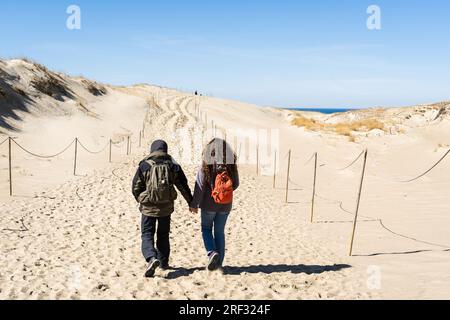 Ein paar Rucksacktouristen gehen Hand in Hand entlang der hügeligen Sanddünen an der Kurischen Nehrung, Litauen. Stockfoto