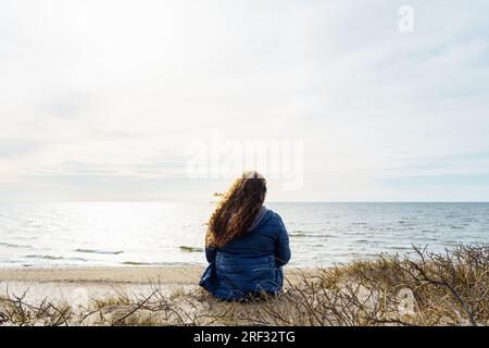 Langhaarige, lockige Frau in Übergröße am Meer, Rückansicht. Stockfoto