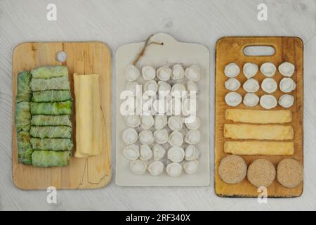 Verschiedene hausgemachte Halbzeuge auf Holzbrett. Gefrorene Schnitzel, Klöße, Kohlbrötchen und Pfannkuchen. Zubereitungen selbstgemachter Lebensmittel. Stockfoto