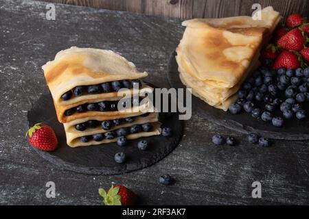 Foto zwischen dünnen Pfannkuchen liegen Blaubeeren auf einem Steinbrett, Erdbeeren liegen daneben Stockfoto