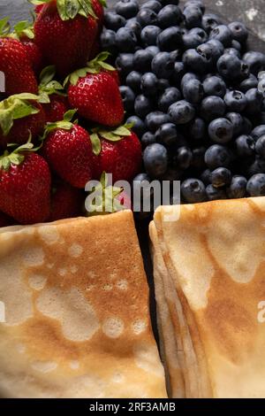 Foto von gebratenen, dünnen Pfannkuchen mit frischen, reifen, saftigen Erdbeeren und Blaubeeren aus nächster Nähe Stockfoto