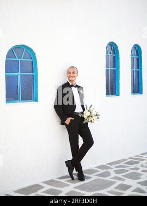 Stilvoller Bräutigam wartet vor der Kirche auf die Braut mit einem Blumenstrauß Stockfoto