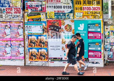 Menschen, die an Immobilien- und Werbeplakaten auf der Stadtmauer vorbeigehen, Hongkong, SAR, China Stockfoto