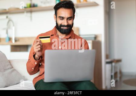 Arabischer Mann mit Laptop und Kreditkarte, der im Haus bezahlt Stockfoto