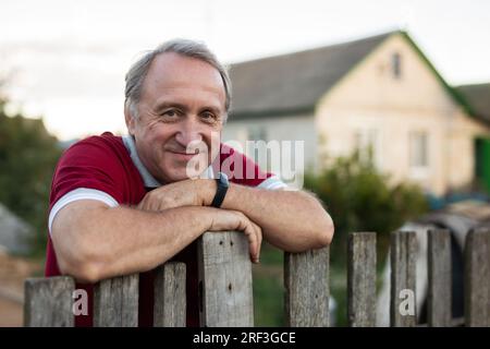 Ein erwachsener Mann, der entspannt neben dem Zaun im Garten steht und lächelt Stockfoto