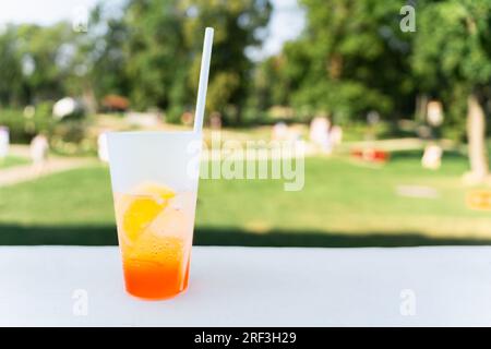 Ein Glas mit einem Aperal Spritz Cocktail, ein Stück Orange und ein Stroh im Park im Sommer. Stockfoto