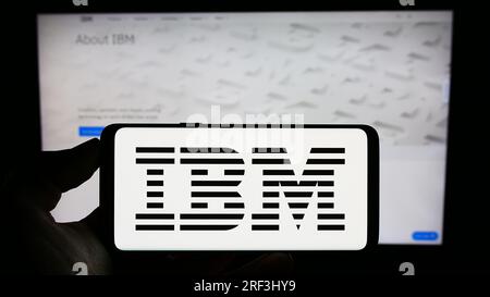 Person, die ein Mobiltelefon mit dem Logo der International Business Machines Corporation (IBM) auf dem Bildschirm vor der Webseite hält. Konzentrieren Sie sich auf das Display des Telefons. Stockfoto