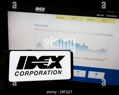 Person, die ein Mobiltelefon mit dem Logo des amerikanischen Fertigungsunternehmens IDEX Corporation auf dem Bildschirm vor der Webseite hält. Konzentrieren Sie sich auf das Display des Telefons. Stockfoto