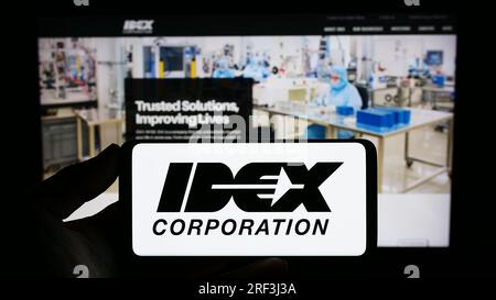 Person, die ein Mobiltelefon mit dem Logo des US-amerikanischen Fertigungsunternehmens IDEX Corporation auf dem Bildschirm vor der Unternehmenswebseite hält. Konzentrieren Sie sich auf das Display des Telefons. Stockfoto