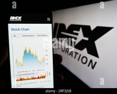 Person, die ein Mobiltelefon mit einer Webseite des US-amerikanischen Fertigungsunternehmens IDEX Corporation auf dem Bildschirm vor dem Logo hält. Konzentrieren Sie sich auf die Mitte des Telefondisplays. Stockfoto