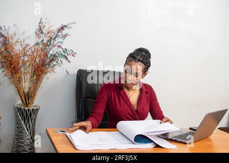 Wunderschöne junge afrikanerin, die in ihrem Büro mit Arbeit beschäftigt ist Stockfoto