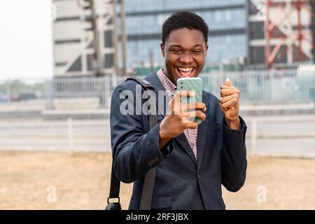 Ein junger afrikaner schaut aufs Telefon und freut sich Stockfoto