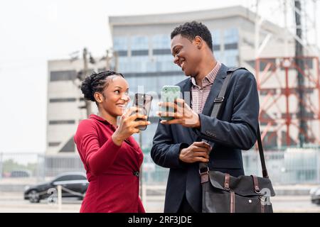Aufgeregter junger afrikaner und junge afrikanerin checken ihre Telefone Stockfoto
