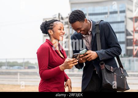 Junge afrikanische Geschäftsleute, die draußen auf ihrem Telefon telefonieren, sich unterhalten und lachen Stockfoto