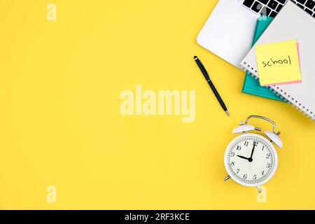 Laptop, Wecker und Notizblöcke auf gelbem Hintergrund. Stockfoto