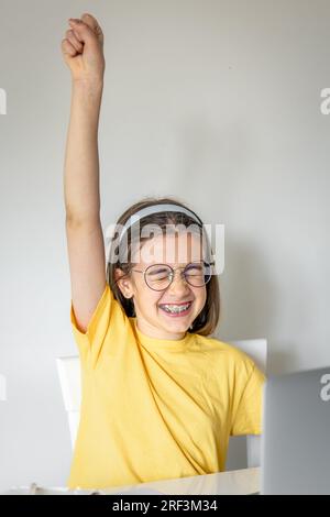 Süßes Schulmädchen mit einem Laptop, das zu Hause lernt, online lernt. Stockfoto