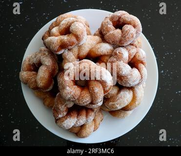Frisch zubereitete Zucker-Donuts auf einem weißen Essteller auf einer schwarzen Granitoberfläche Stockfoto