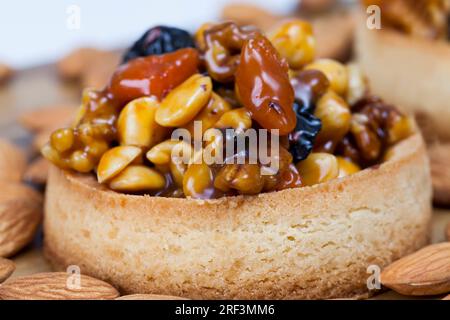 Weizentörtchen mit süßer Füllung, knusprige Törtchen mit Haselnüssen, Erdnüssen und anderen Zutaten, Weizenteig Törtchen mit Nüssen und getrockneten Früchten in Crea Stockfoto