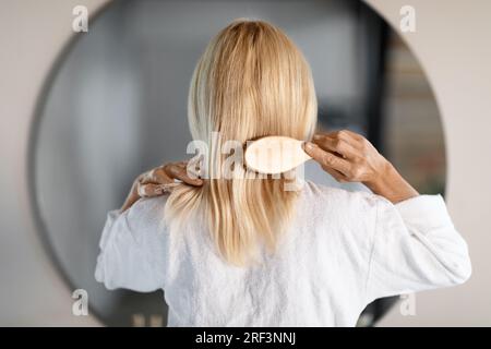 Rückansicht Der „Mature Woman“, Die Zu Hause Haare Mit Einer Bambusbürste Kämmt Stockfoto