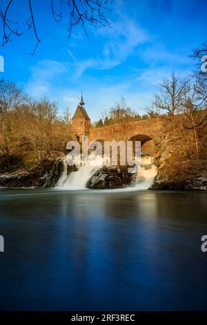Pyrmont Mill in Rheinland-Pfalz Deutschland Steinbrücke mit Wasserfall, See und Fachwerkhaus. Eine Burgruine im Hintergrund Stockfoto