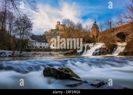 Pyrmont Mill in Rheinland-Pfalz Deutschland Steinbrücke mit Wasserfall, See und Fachwerkhaus. Eine Burgruine im Hintergrund Stockfoto