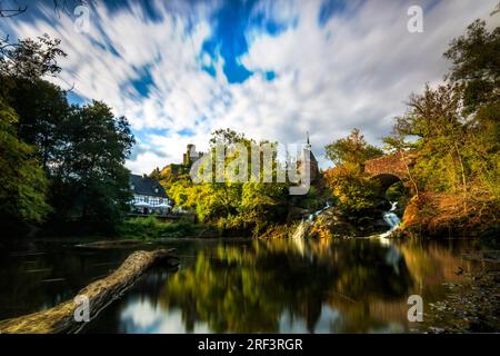 Pyrmont Mill in Rheinland-Pfalz Deutschland Steinbrücke mit Wasserfall, See und Fachwerkhaus. Eine Burgruine im Hintergrund Stockfoto
