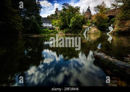 Pyrmont Mill in Rheinland-Pfalz Deutschland Steinbrücke mit Wasserfall, See und Fachwerkhaus. Eine Burgruine im Hintergrund Stockfoto