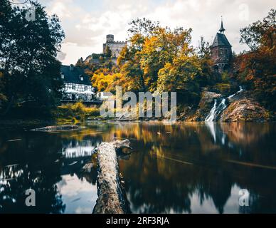 Pyrmont Mill in Rheinland-Pfalz Deutschland Steinbrücke mit Wasserfall, See und Fachwerkhaus. Eine Burgruine im Hintergrund Stockfoto