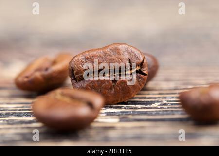Kaffeebohnen, aus denen man ein heißes belebendes Kaffeegetränk zubereiten kann, braune Kaffeebohnen, die auf einem Tisch aus Brettern liegen Stockfoto