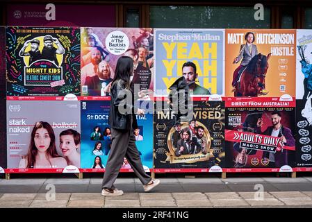 Junge Frau, die auf Werbeplakaten für Shows beim Edinburgh Fringe Festival in George Square, Edinburgh, Schottland, Großbritannien, vorbeigeht. Stockfoto