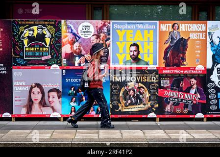 Junge Frau, die auf Werbeplakaten für Shows beim Edinburgh Fringe Festival in George Square, Edinburgh, Schottland, Großbritannien, vorbeigeht. Stockfoto