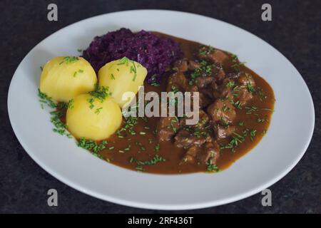 Köstliches Essen - Gulasch aus einer Gamois-Jährlichkeit mit Kartoffeln und Rotkohl, brauner Sauce und Schnittlauch Stockfoto