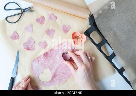 Der Koch schneidet einen herzförmigen Wurst-Schinken, der auf Pergament geschnitten wurde, von oben auf einem Pizza-Deco-Hintergrund. Pizza zum Valentinstag kochen Stockfoto