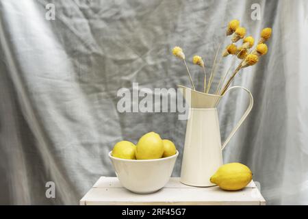 Stillleben mit einer emaillierten Blechkanne mit getrockneten Blumen und einer weißen Schüssel mit reifen Zitronen Stockfoto