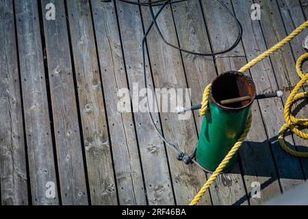 Gelbes Anlegeseil, das sicher an einer grünen Metallklampe auf einem Holzdock befestigt ist Stockfoto