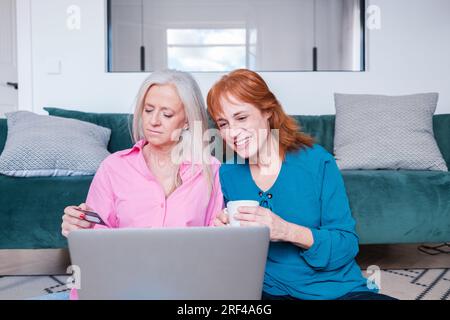Ein paar Frauen mittleren Alters, die zu Hause im Internet einkaufen. Konzept: Lifestyle, Shopping, zusammen Stockfoto