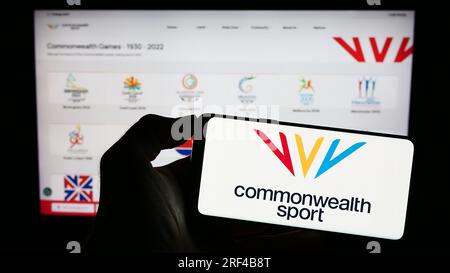 Person, die ein Mobiltelefon mit dem Logo der Organisation Commonwealth Games Federation (CGF) auf dem Bildschirm vor der Webseite hält. Konzentrieren Sie sich auf das Display des Telefons. Stockfoto