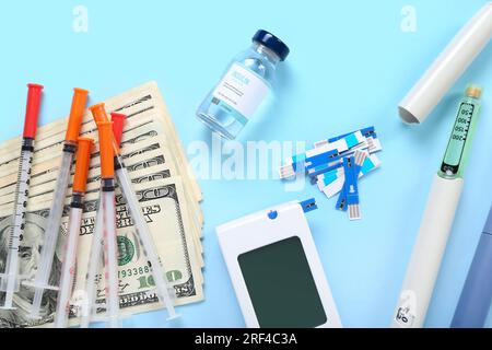 Insulin mit Glukosimeter, Lanzettenstiften, Spritzen und Geld auf blauem Hintergrund. Teures Medizinkonzept Stockfoto