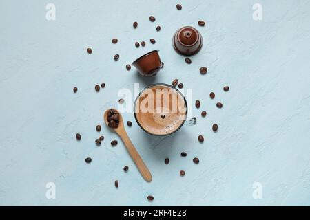 Tasse köstlicher Kaffee, Holzlöffel, Bohnen und Kapseln auf einem blauen Tisch Stockfoto