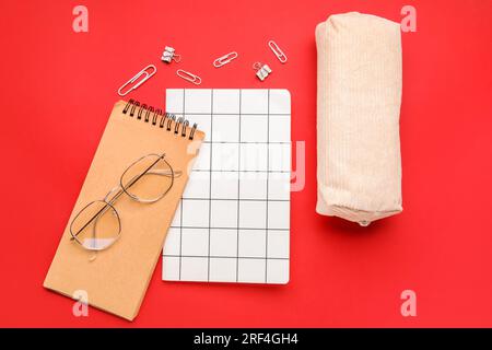 Komposition mit Notizbüchern, Federmäppchen und Brillen auf rotem Hintergrund Stockfoto