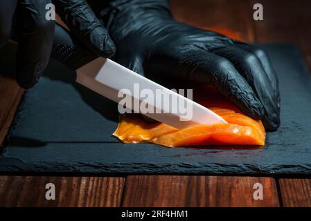 Der Koch schneidet Lachsfilet mit dem Messer auf dem schwarzen Brett in der professionellen Küche Stockfoto