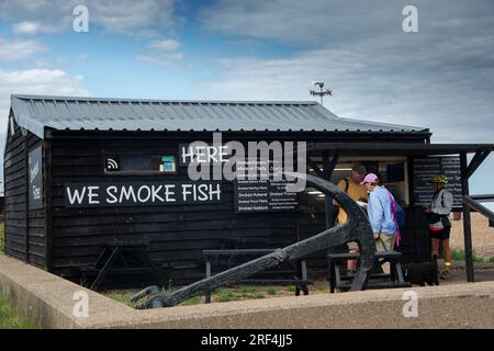 Kunden, die in einem traditionellen Fischrauchhaus am Kieselstrand in der touristischen Küstenstadt Aldeburgh an der Suffolk Coast, England, kaufen Stockfoto